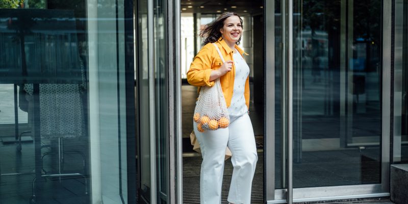 Size-inclusive body positivity advocates for acceptance and celebration of all body sizes and shapes, including plus-size or overweight. Happy curvy young woman in yellow cloth on city street.